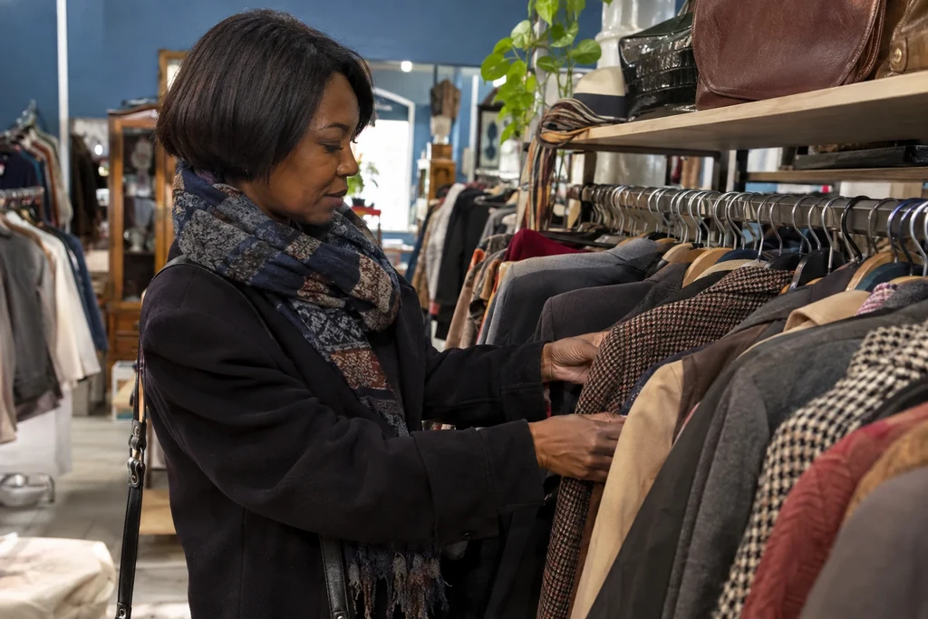 Une femme examine des vestes sur un portant dans une boutique de vêtements d’occasion.