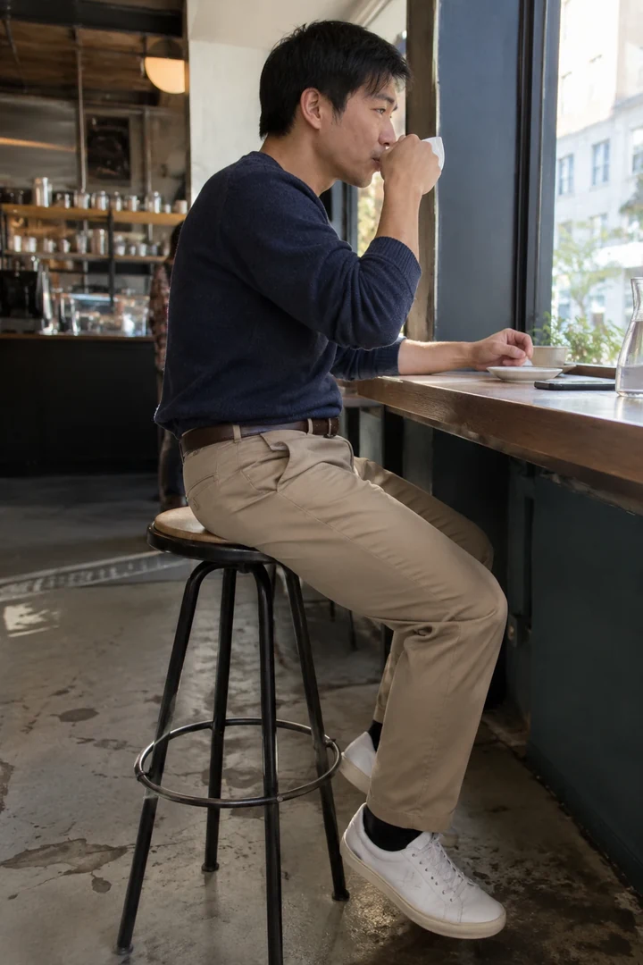 Un homme assis sur un tabouret de café porte un chino avec une ceinture discrète.