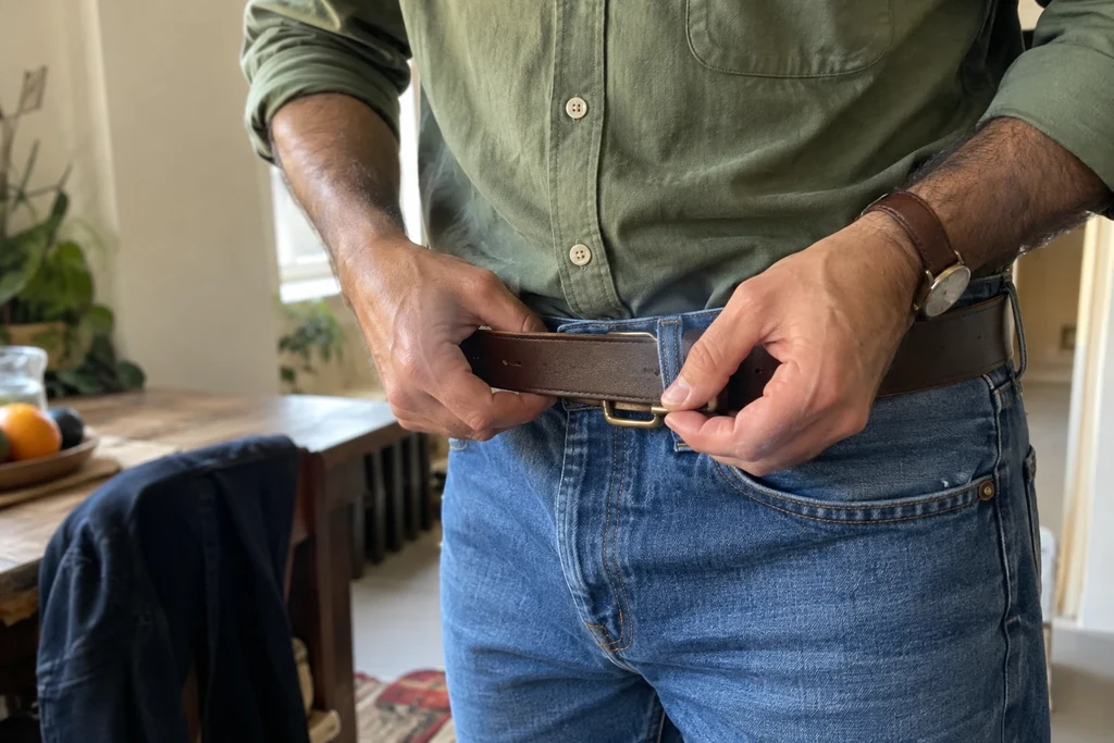 Des mains font passer une ceinture simple dans les passants d’un jean.