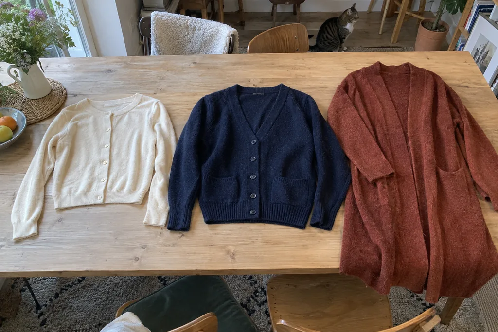 Trois cardigans écru, marine et rouille posés à plat, de longueurs différentes.