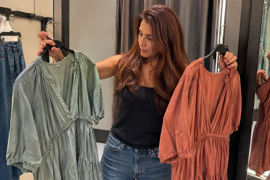 Une femme compare deux vêtements de couleurs différentes sur leurs cintres dans une cabine.