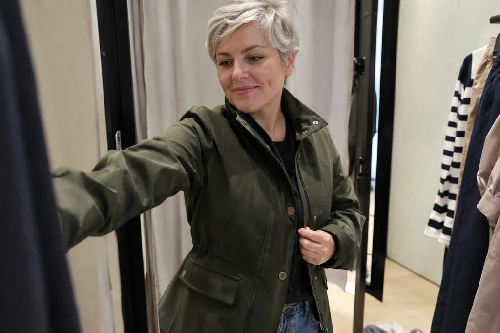 Une femme en veste unie avance les bras dans une cabine d’essayage.