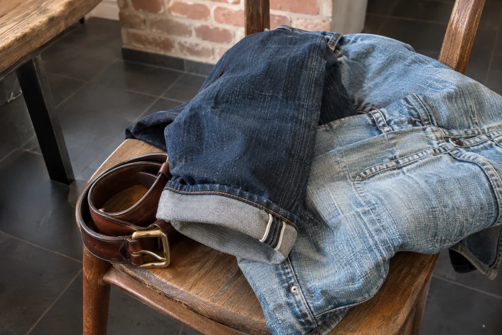 Un revers de denim foncé est posé près d’un tissu délavé et d’une ceinture brune.