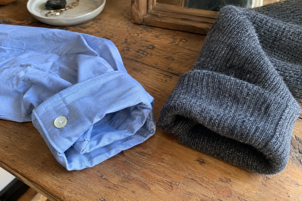 Un poignet de chemise et une manche de pull sont posés sur une table en bois.