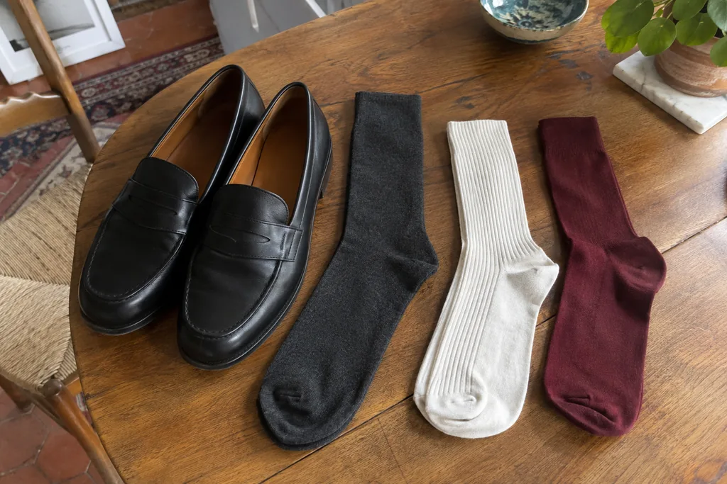 Chaussettes gris foncé, écrues et bordeaux posées à côté de mocassins noirs sur une table.