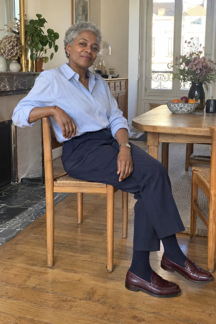 Femme assise en chemise bleu clair, pantalon marine et mocassins bordeaux avec des chaussettes marine.