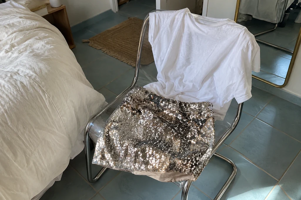 Une jupe à paillettes et un tee-shirt uni sont posés sur une chaise de chambre.