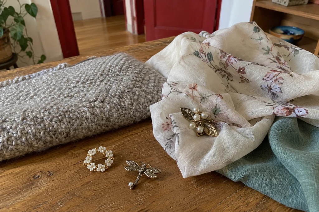Trois petites broches sont posées près d’un tissu épais et d’une étoffe plus délicate sur une table.