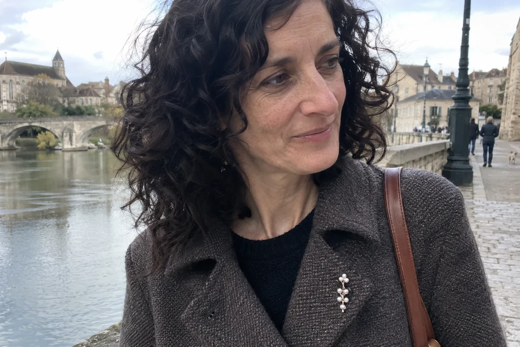 Une femme porte une petite broche discrète sur le revers d’une veste unie dans la rue.