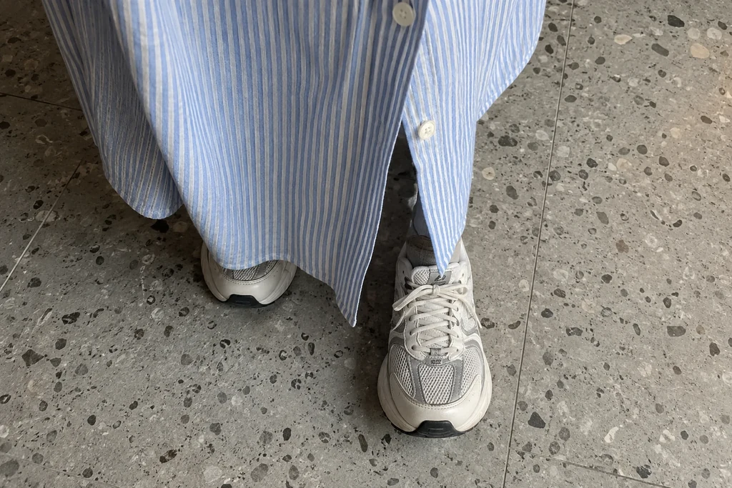 Le bas boutonné d’une robe chemise et des baskets sont visibles pendant un petit pas.