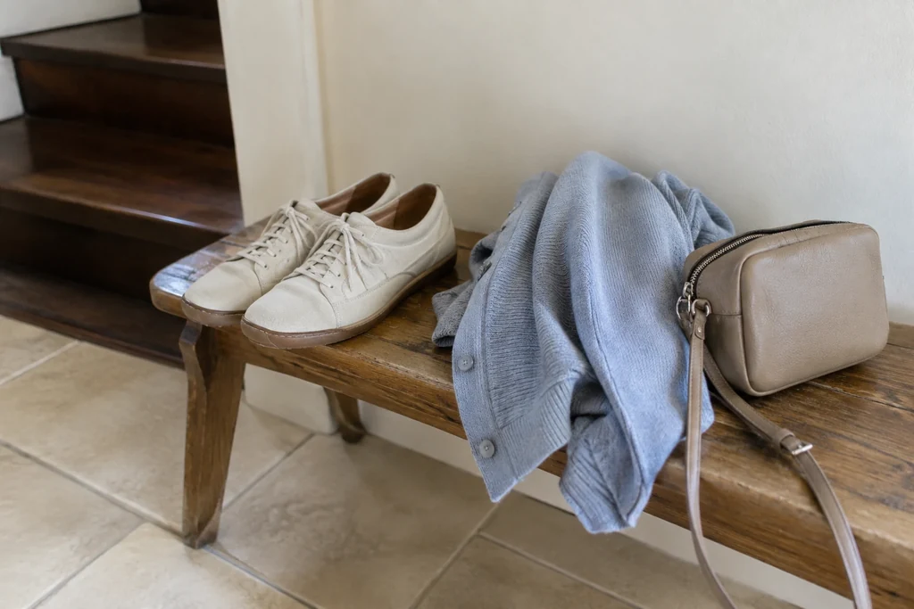 Des chaussures basses, un cardigan fin et un petit sac sont posés sur un banc à la maison.