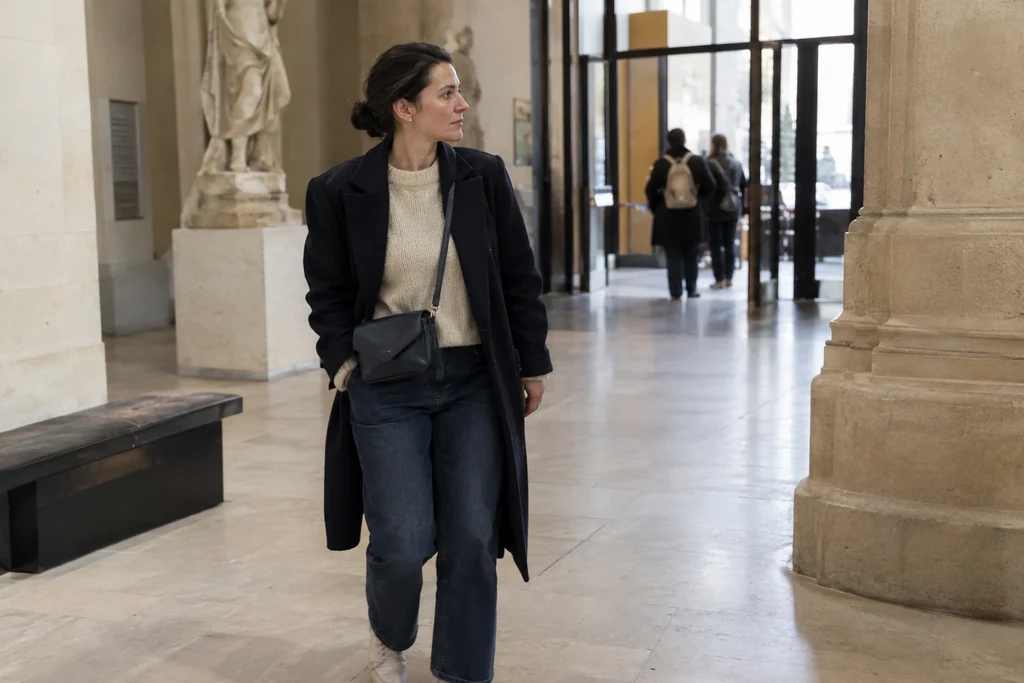 Une femme en tenue simple superposée porte un petit sac fermé à l’entrée d’un musée.