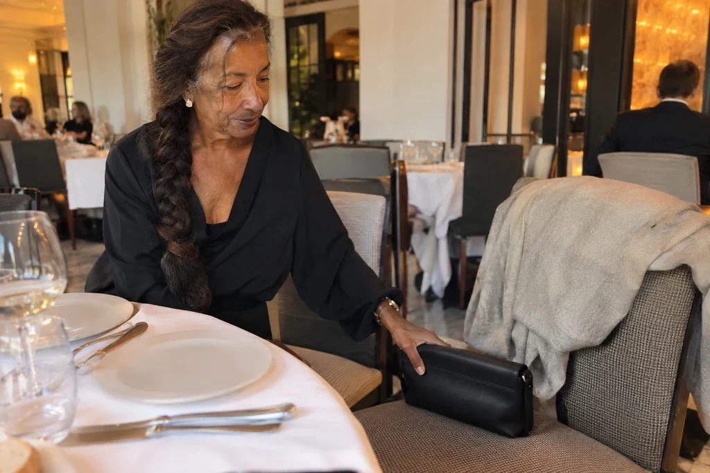 Une femme place un petit sac fermé près d’un manteau sur une chaise vide au restaurant.