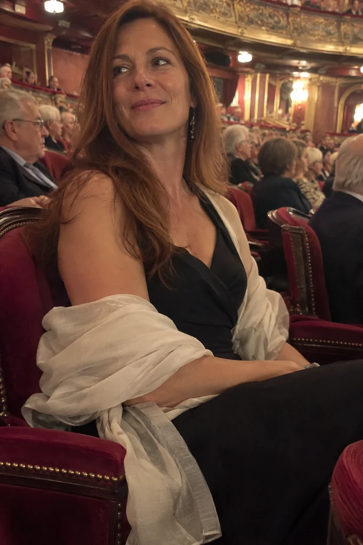 Une femme en robe sombre et étole claire est assise dans un fauteuil de théâtre avant le spectacle.