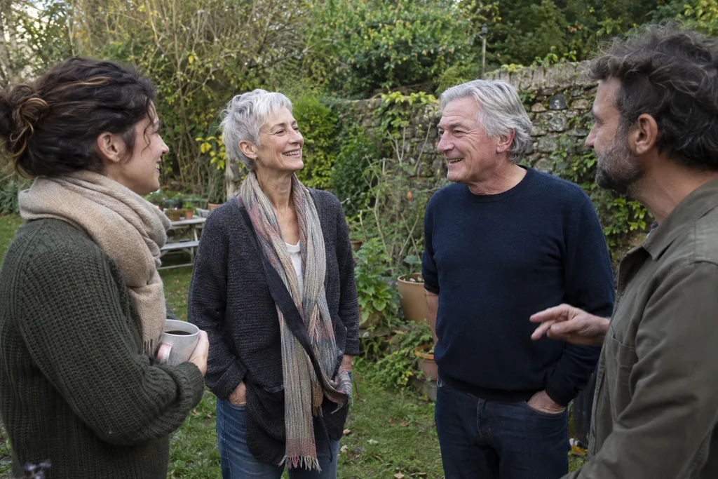 Quatre adultes d’âges différents discutent dans un jardin avec des vêtements de tons variés et doux.